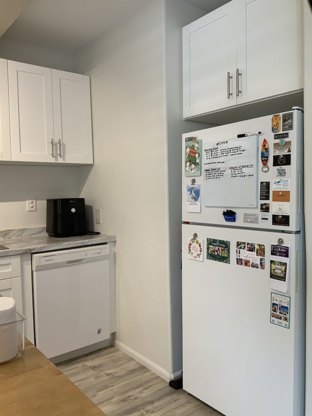 kitchen featuring white appliances, baseboards, white cabinets, light countertops, and light wood-style floors