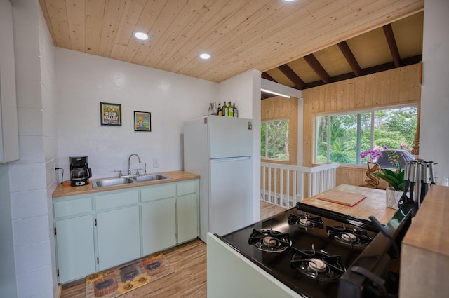 kitchen with white fridge, light wood-type flooring, vaulted ceiling with beams, range, and sink