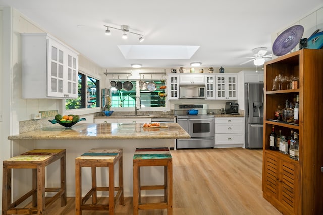 kitchen with a breakfast bar area, appliances with stainless steel finishes, white cabinetry, a skylight, and kitchen peninsula