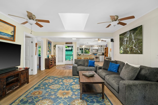 living room with ceiling fan, a skylight, and light wood-type flooring