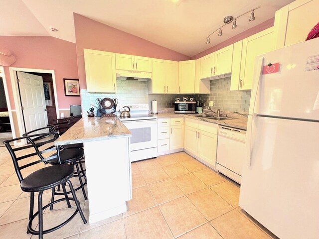 kitchen featuring light tile patterned floors, white appliances, a breakfast bar, vaulted ceiling, and kitchen peninsula