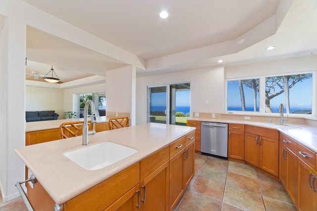 kitchen with stainless steel dishwasher, sink, a tray ceiling, and a kitchen island with sink