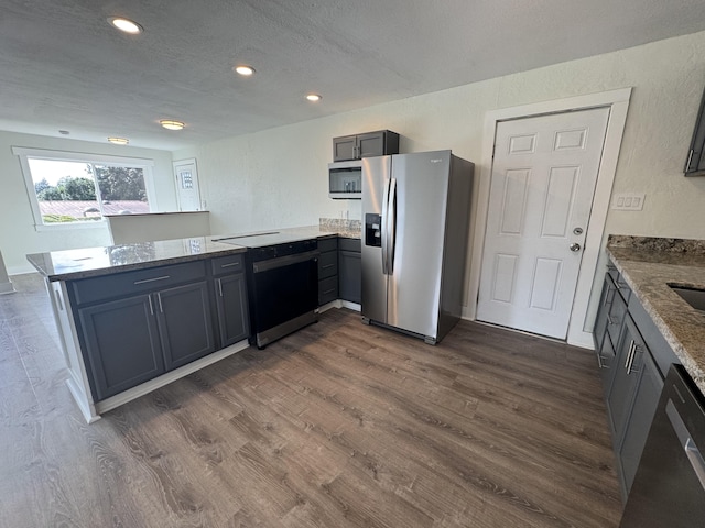 kitchen featuring light stone counters, appliances with stainless steel finishes, kitchen peninsula, and dark wood-type flooring