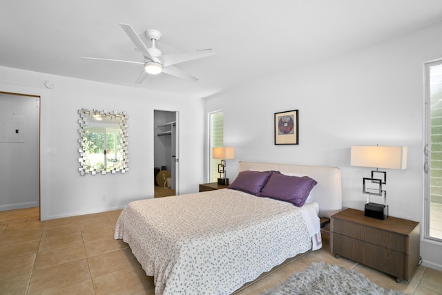 bedroom with light tile patterned floors, baseboards, a ceiling fan, ensuite bath, and a walk in closet