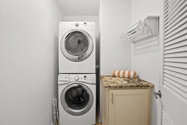 laundry area featuring stacked washer / dryer and cabinet space