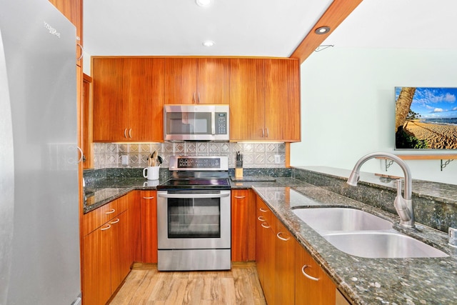 kitchen with stainless steel appliances, tasteful backsplash, dark stone counters, light hardwood / wood-style flooring, and sink