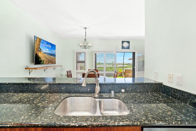 kitchen featuring an inviting chandelier, kitchen peninsula, dark stone counters, pendant lighting, and sink