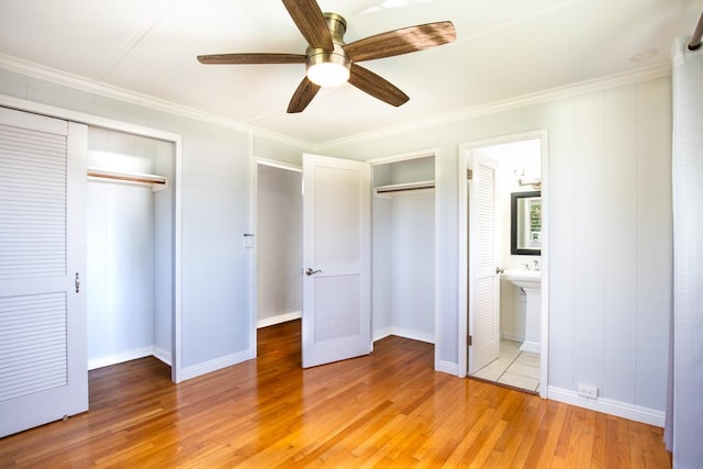 unfurnished bedroom featuring ceiling fan, two closets, light hardwood / wood-style flooring, ornamental molding, and connected bathroom