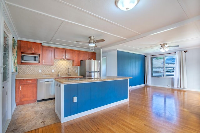 kitchen featuring ceiling fan, stainless steel appliances, tasteful backsplash, light wood-type flooring, and a center island