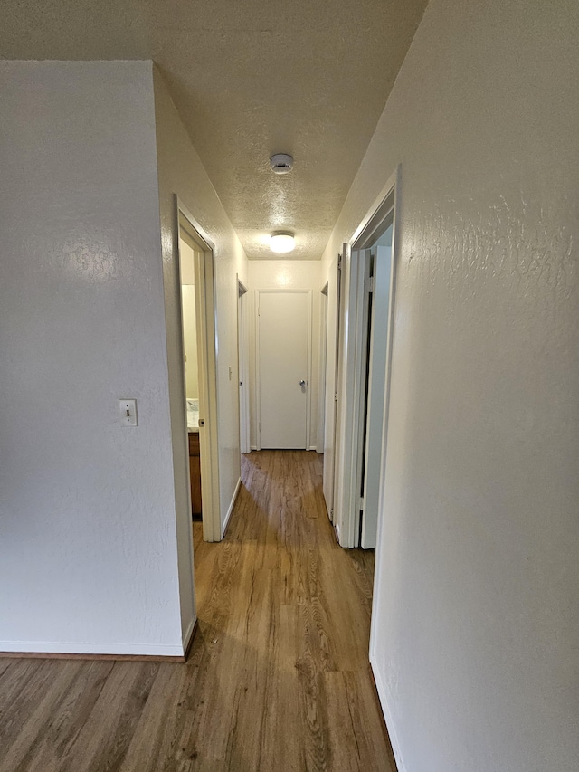 hall with light hardwood / wood-style floors and a textured ceiling