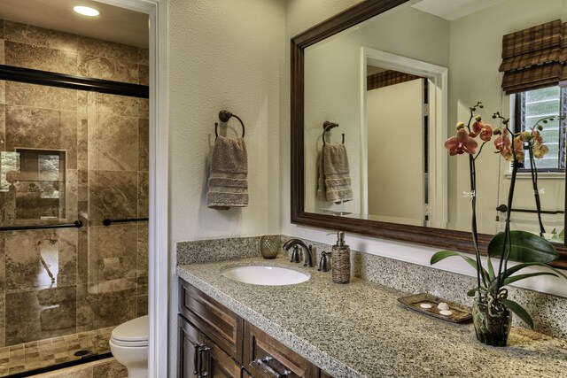 bathroom featuring a shower with door, vanity, and toilet