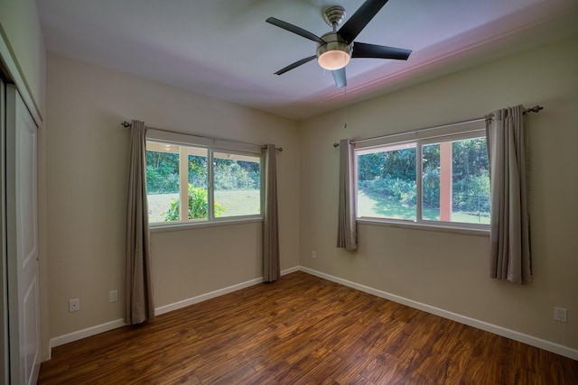 spare room featuring a healthy amount of sunlight, dark wood-type flooring, and ceiling fan