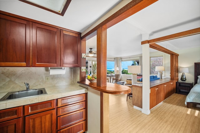 kitchen featuring sink, backsplash, kitchen peninsula, ceiling fan, and light hardwood / wood-style flooring