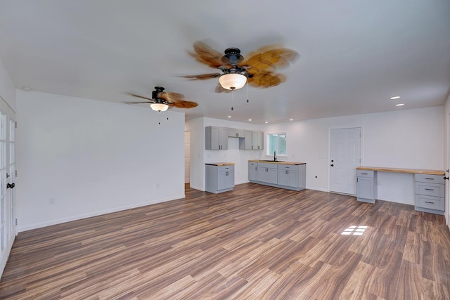 unfurnished living room with dark wood-type flooring, ceiling fan, built in desk, and sink