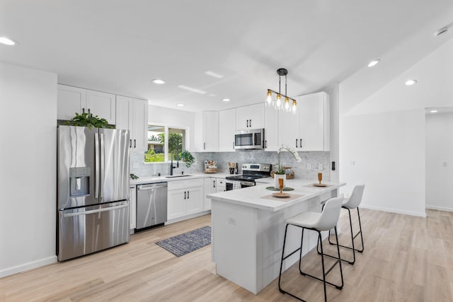 kitchen featuring a breakfast bar, sink, white cabinetry, decorative light fixtures, and stainless steel appliances