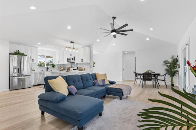 living room featuring light hardwood / wood-style flooring, sink, ceiling fan with notable chandelier, and vaulted ceiling