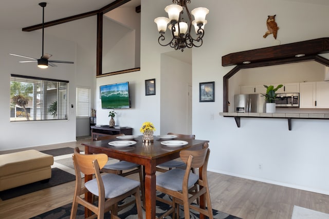 dining room with a towering ceiling, ceiling fan with notable chandelier, and light hardwood / wood-style flooring