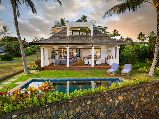 back house at dusk featuring an outbuilding, a swimming pool side deck, an outdoor living space, and a lawn