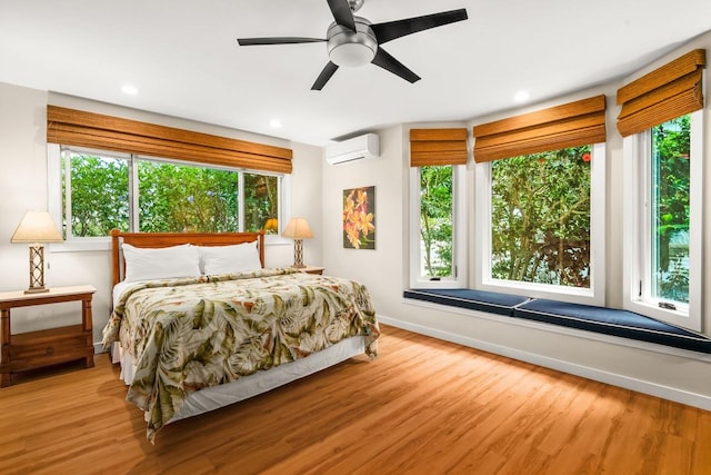 bedroom with ceiling fan, light hardwood / wood-style floors, multiple windows, and a wall mounted air conditioner