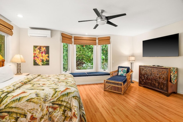 bedroom with ceiling fan, hardwood / wood-style flooring, an AC wall unit, and multiple windows