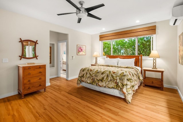 bedroom featuring ceiling fan, ensuite bath, a wall unit AC, and light wood-type flooring