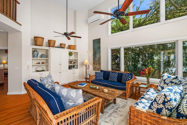 living room with ceiling fan, light hardwood / wood-style flooring, a wall unit AC, and a towering ceiling