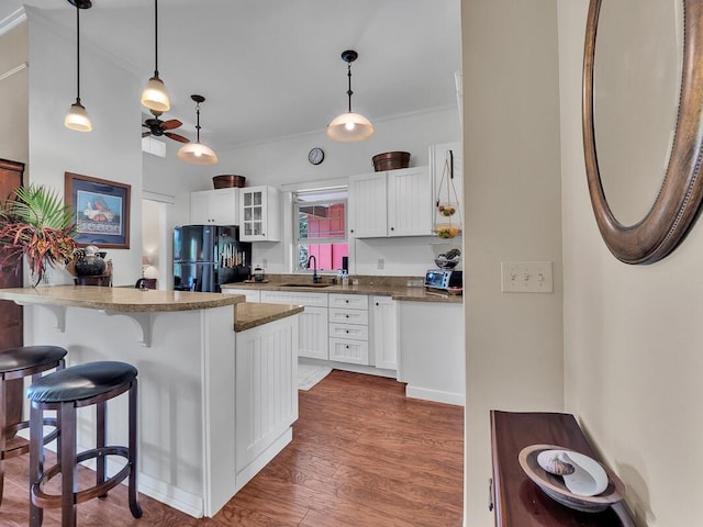 kitchen with sink, dark wood-type flooring, black refrigerator, white cabinets, and decorative light fixtures