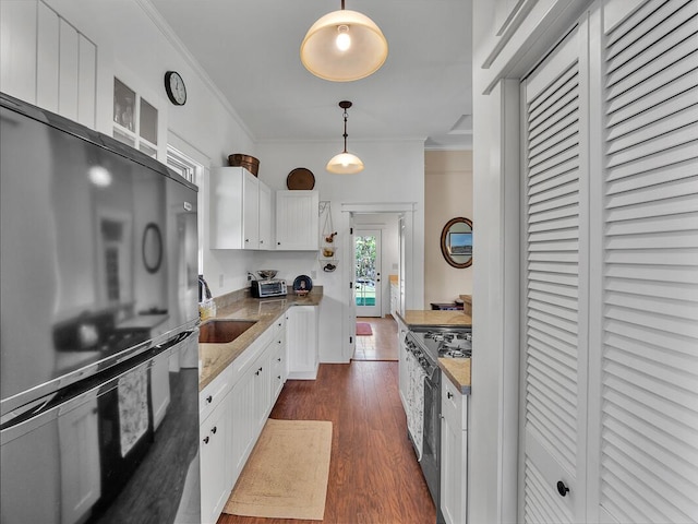 kitchen with stainless steel range oven, sink, black fridge, pendant lighting, and white cabinets