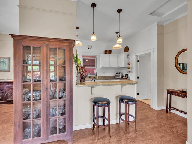 kitchen with a breakfast bar, white cabinetry, light stone counters, decorative light fixtures, and kitchen peninsula