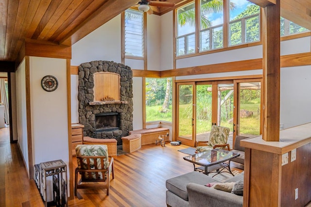 living room with hardwood / wood-style floors, a towering ceiling, a stone fireplace, ceiling fan, and wooden ceiling