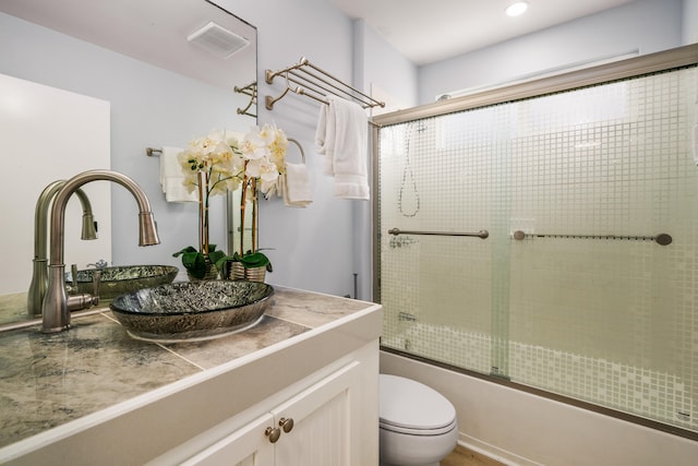 full bathroom featuring toilet, bath / shower combo with glass door, and vanity