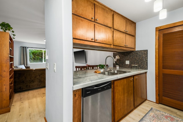 kitchen featuring stainless steel dishwasher, backsplash, sink, and light wood-type flooring