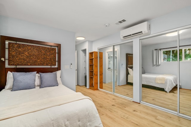 bedroom with two closets, hardwood / wood-style floors, and a wall mounted AC