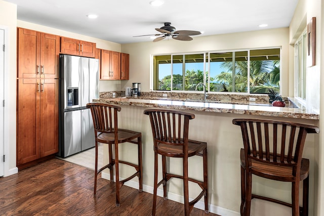 kitchen featuring stainless steel refrigerator with ice dispenser, dark wood-type flooring, a kitchen bar, sink, and light stone countertops