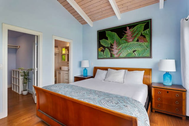 bedroom featuring a walk in closet, ensuite bath, light hardwood / wood-style floors, lofted ceiling with beams, and wooden ceiling