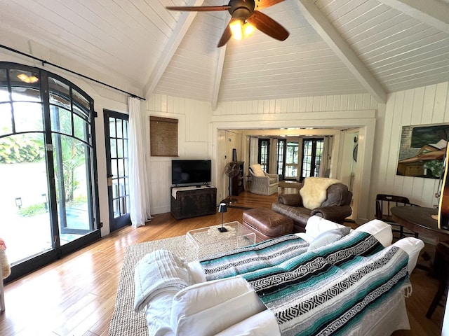 living room featuring lofted ceiling with beams, a healthy amount of sunlight, light wood-type flooring, and wood walls