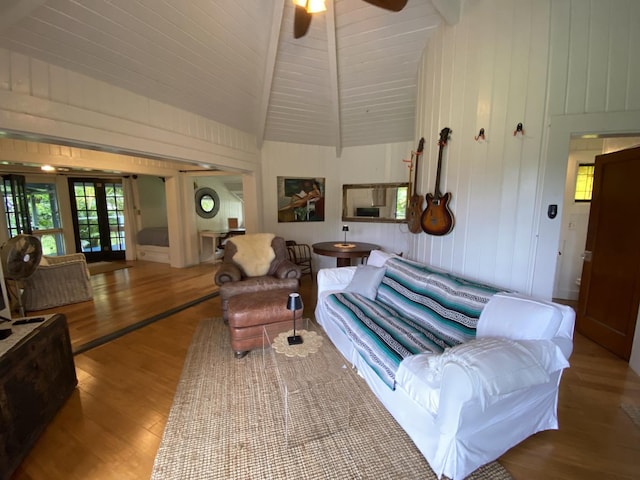 living room featuring ceiling fan, wooden walls, wood-type flooring, lofted ceiling with beams, and french doors