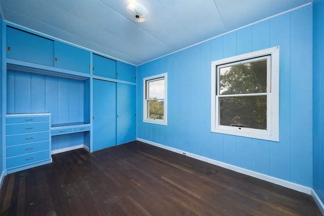 unfurnished bedroom with built in desk and dark hardwood / wood-style flooring