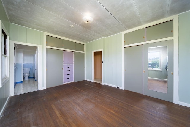 unfurnished bedroom with dark hardwood / wood-style flooring, connected bathroom, and two closets