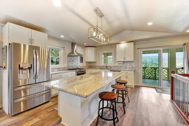 kitchen with lofted ceiling, a kitchen island, white cabinetry, wall chimney range hood, and stainless steel appliances