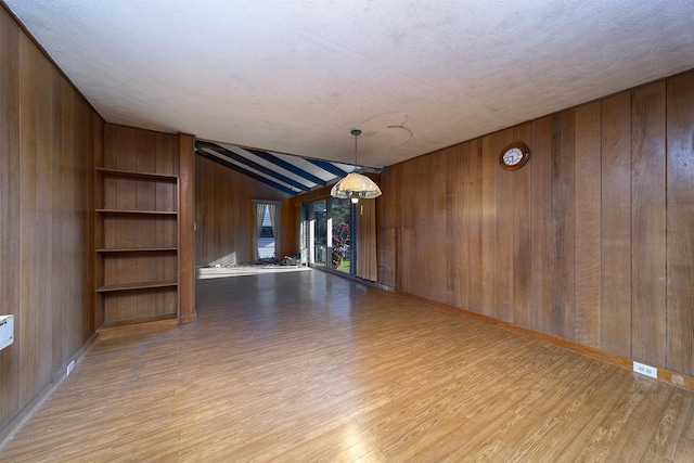 empty room with light hardwood / wood-style flooring, lofted ceiling with beams, a textured ceiling, and wood walls