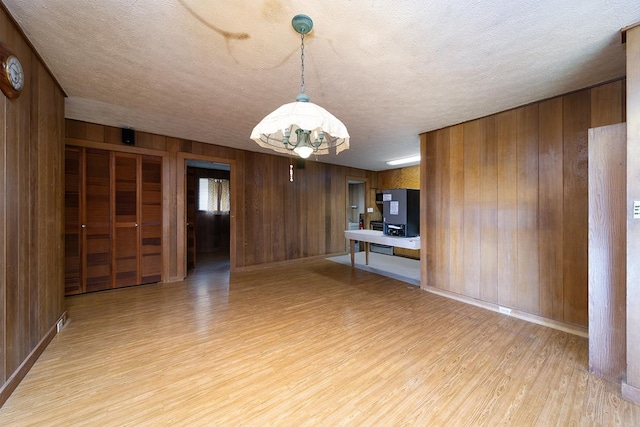 interior space with wooden walls, a textured ceiling, and light hardwood / wood-style flooring