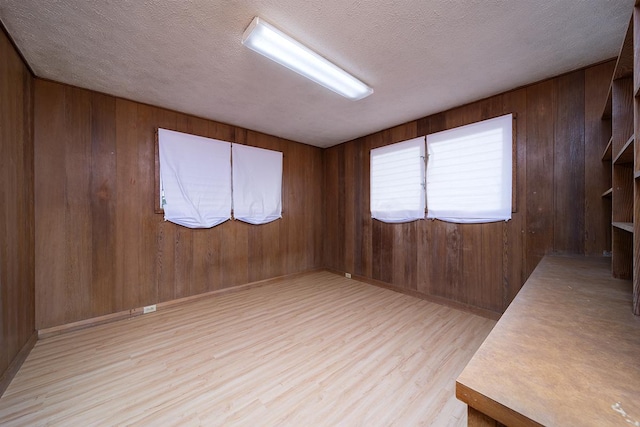 spare room with light hardwood / wood-style floors, a textured ceiling, and wood walls