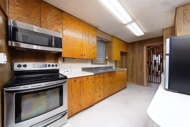 kitchen with appliances with stainless steel finishes, wooden walls, sink, and a textured ceiling