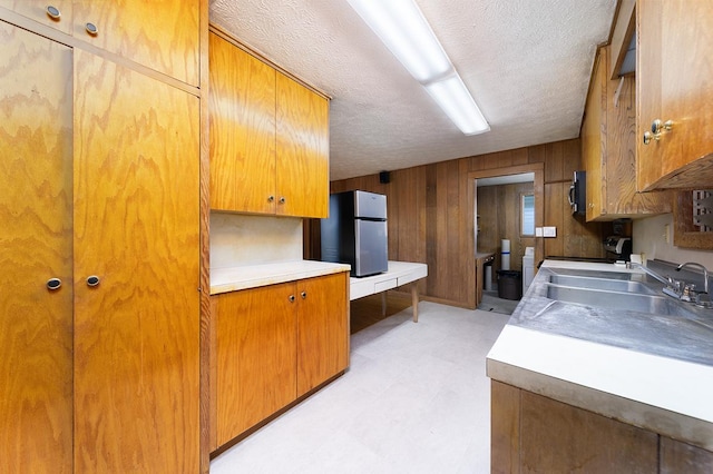 kitchen featuring wooden walls, stainless steel fridge, sink, and a textured ceiling