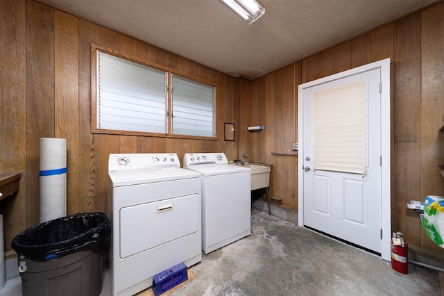 laundry room featuring washing machine and clothes dryer, sink, a textured ceiling, and wood walls