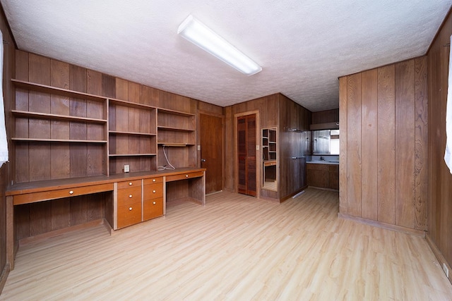 unfurnished office with wooden walls, built in desk, light hardwood / wood-style flooring, and a textured ceiling