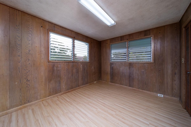 empty room with light hardwood / wood-style floors, a textured ceiling, and wood walls