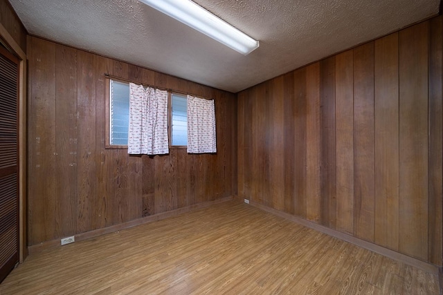 spare room with wood walls, a textured ceiling, and light hardwood / wood-style flooring