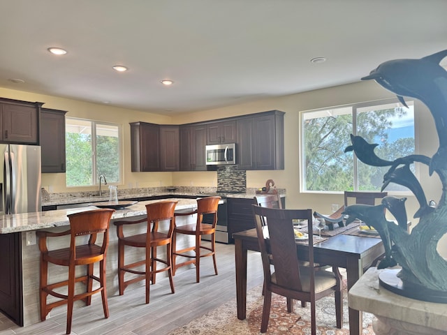 kitchen with appliances with stainless steel finishes, backsplash, light stone counters, light hardwood / wood-style floors, and dark brown cabinets